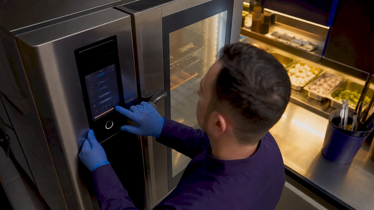 Hands adjusting combi oven controls in kitchen