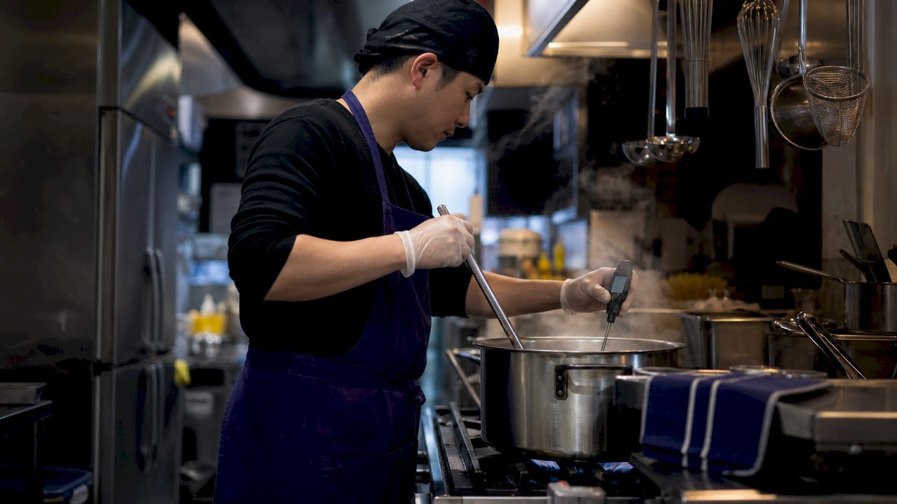 Hands calibrating food thermometer in boiling water pot