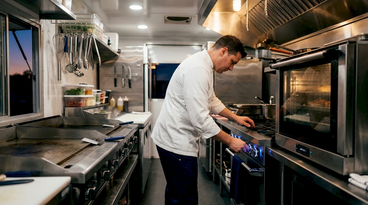 Chef adjusting stove controls inside catering trailer