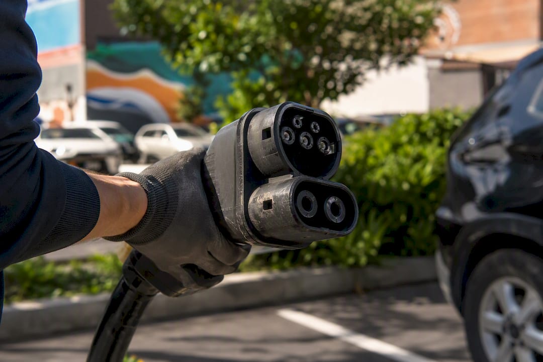 Gloved hand holding bulky CCS EV charging connector