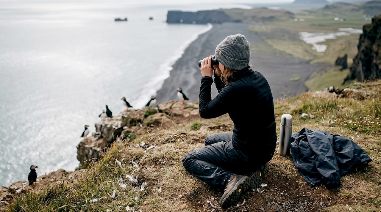 Una donna ammira i puffin dalla scogliera di Dyrhólaey