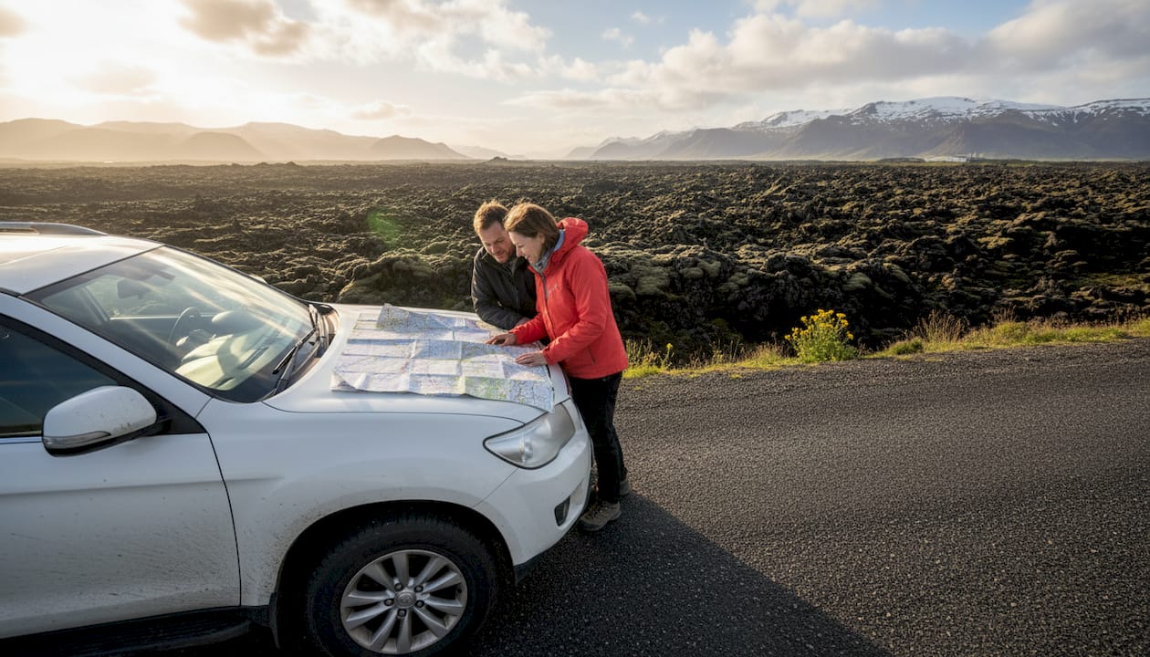 Des voyageurs arrêtés sur une route islandaise, en train d'étudier une carte pour choisir leur prochaine destination.
