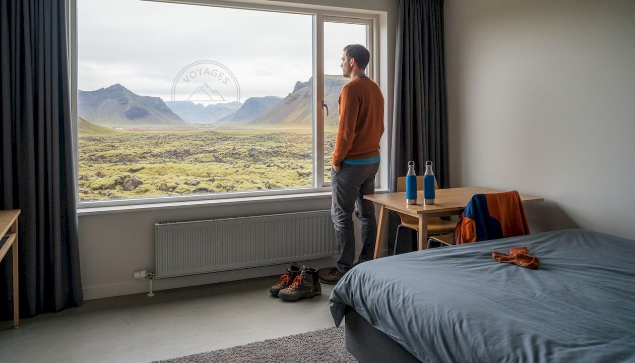 Un homme admire les paysages islandais depuis la fenêtre de sa chambre d’auberge.
