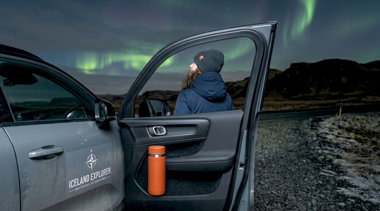 Eine Frau steht unter dem nächtlichen Himmel und bestaunt fasziniert das bunte Schauspiel der Nordlichter.