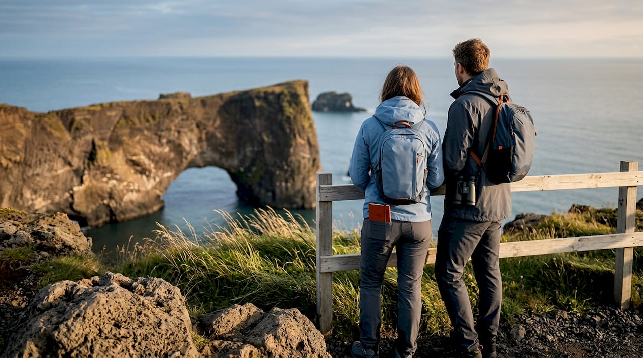 Una pareja contempla el impresionante arco de roca de Dyrhólaey y los acantilados que se extienden junto al mar.
