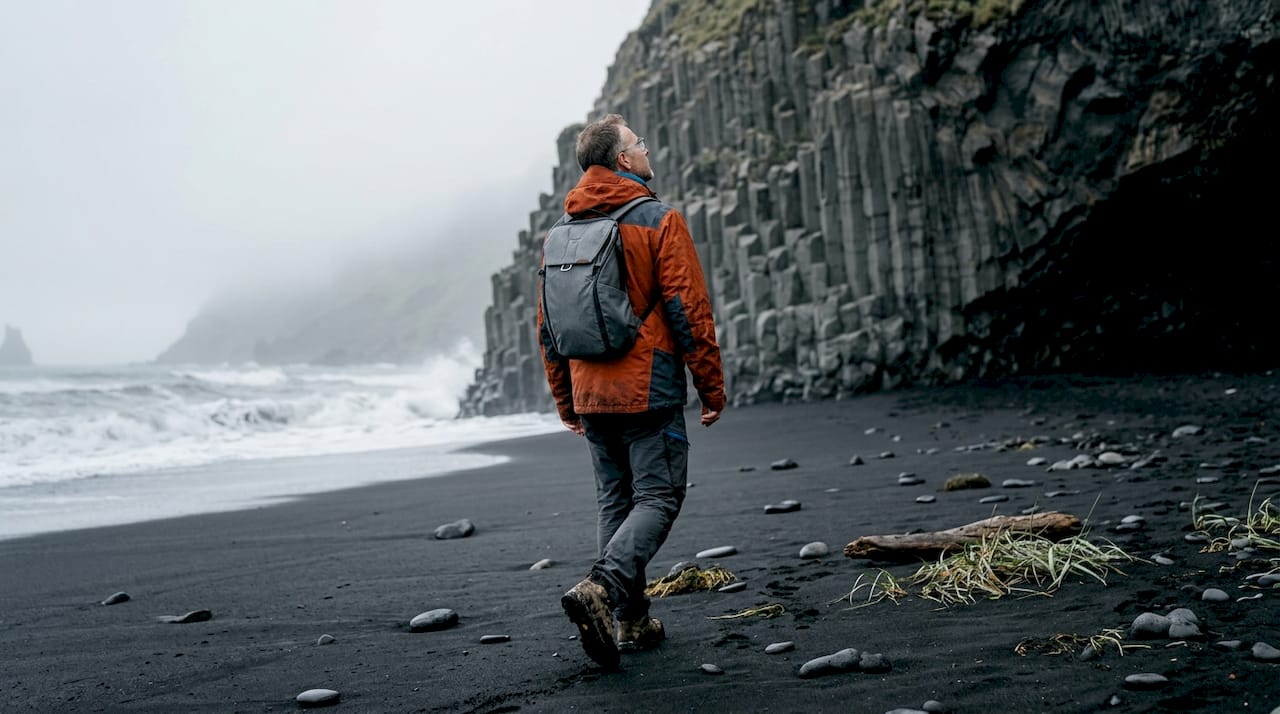 Ein Wanderer legt eine Pause am schwarzen Sandstrand von Reynisfjara ein und genießt den atemberaubenden Ausblick.