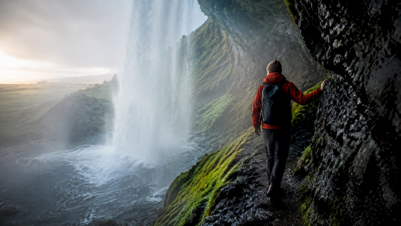 Hiker navigating behind Seljalandsfoss waterfall path