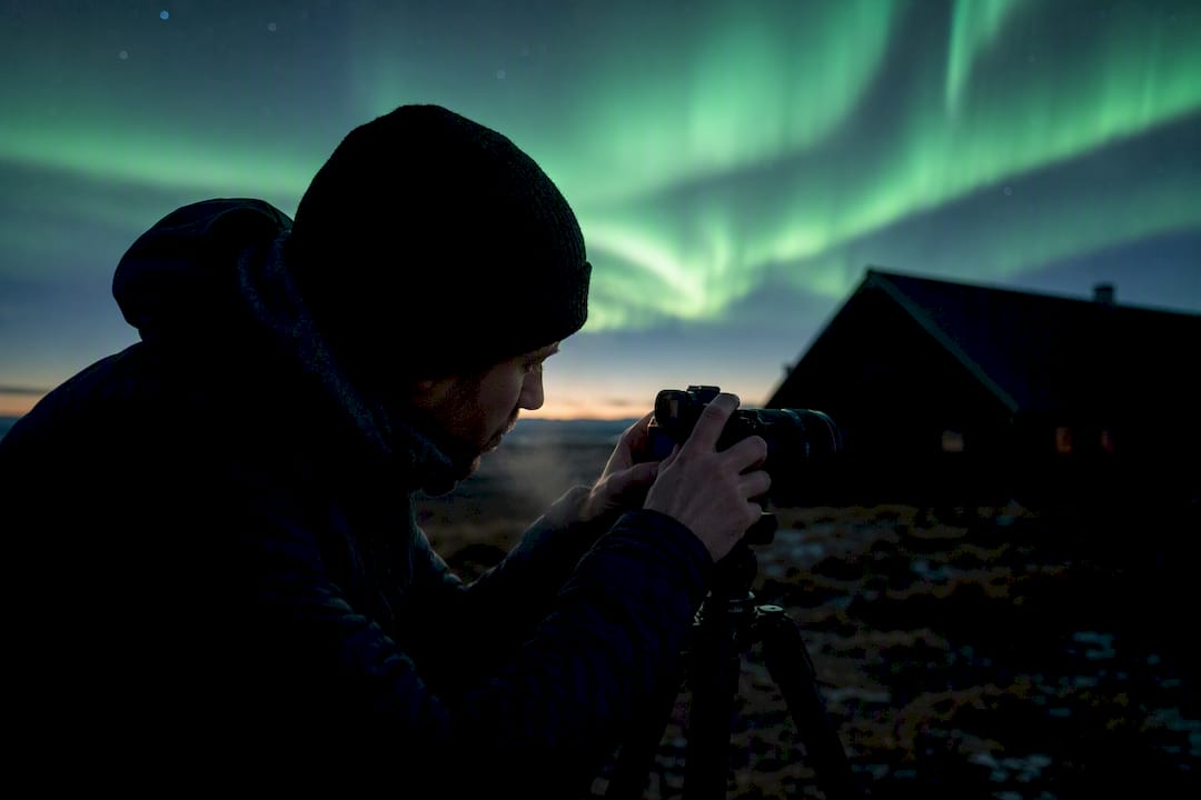 Photographer adjusting camera under northern lights
