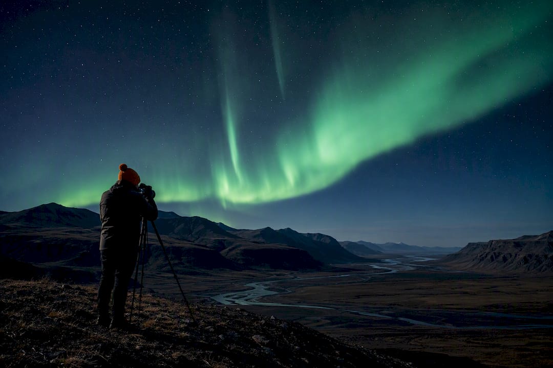 Photographer beneath aurora in Hrífunes
