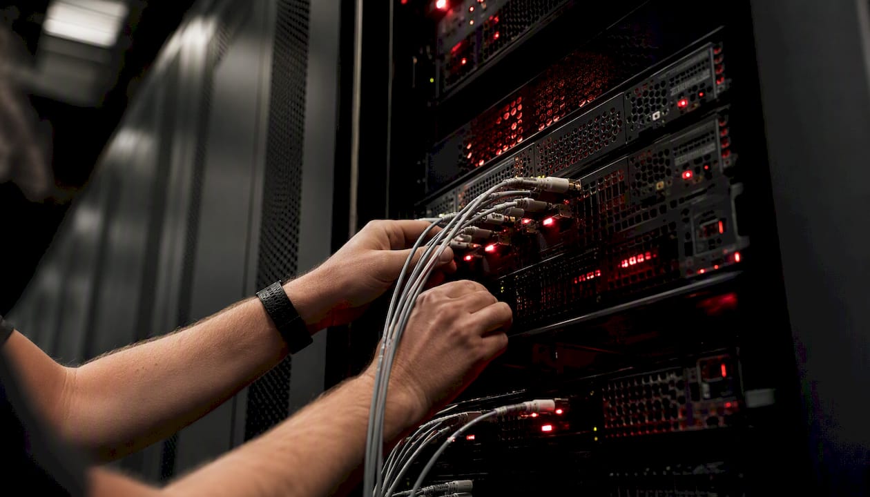 Hands connecting fiber optic cables in datacenter