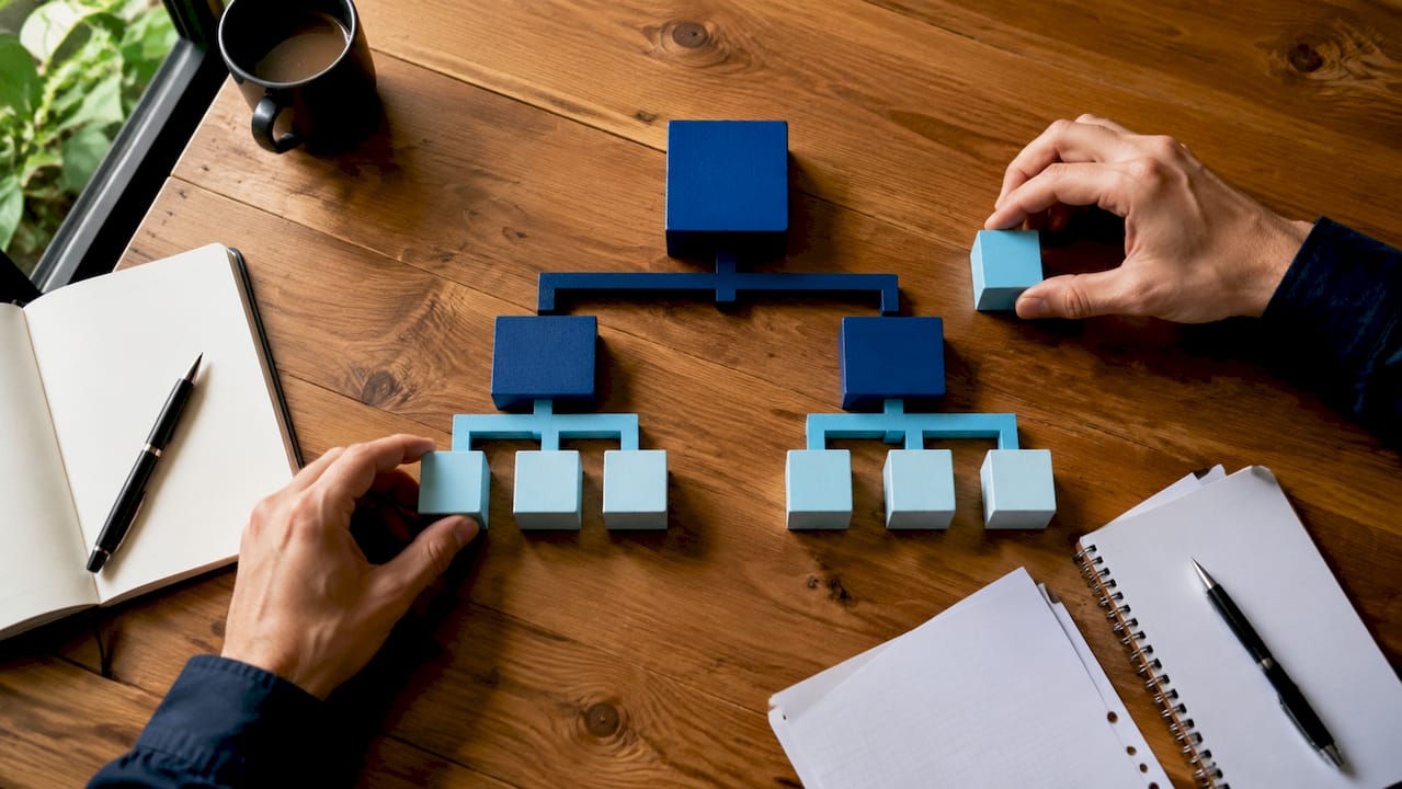 Handen stapelen bouwstenen tot een structuur die een holding symboliseert.