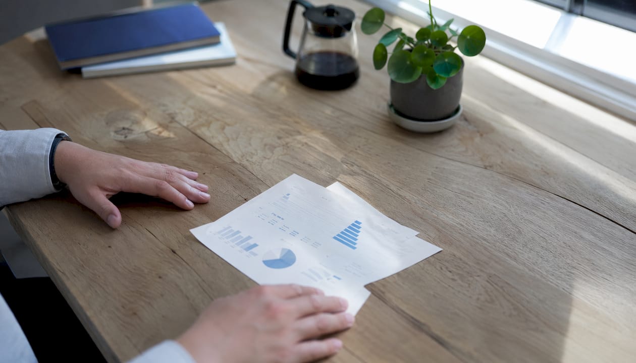 Handen rusten op een tafel met een kamerplant en papieren met duurzaamheidsinformatie