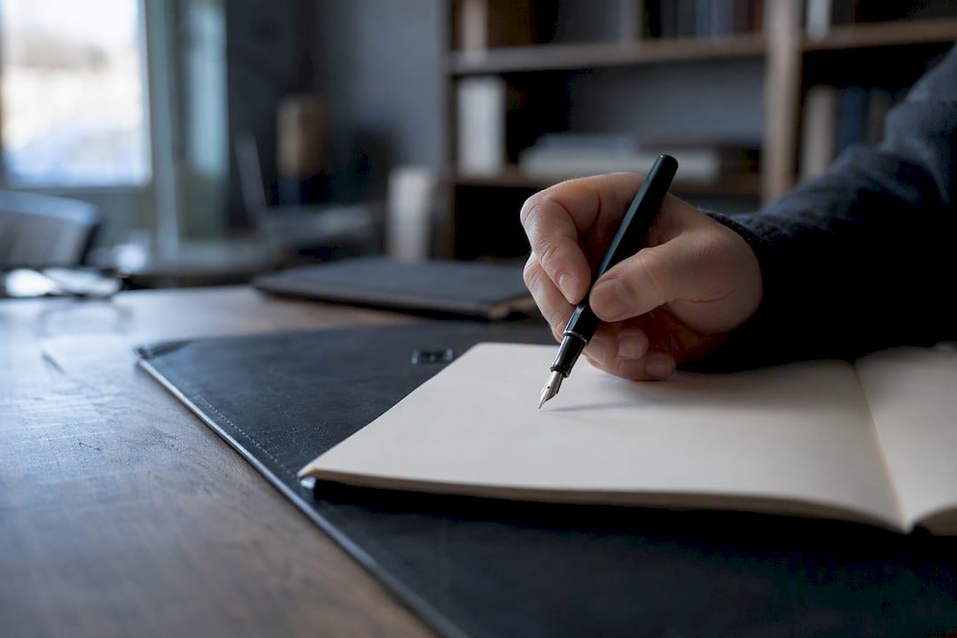 Hand met pen boven een blanco notitieboek
