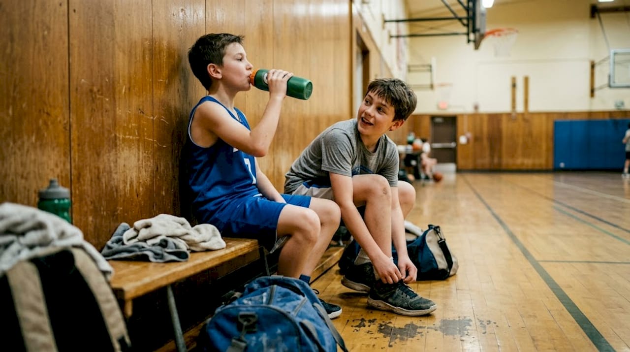 Des jeunes collégiens prennent une pause assis par terre après leur séance de sport au gymnase.