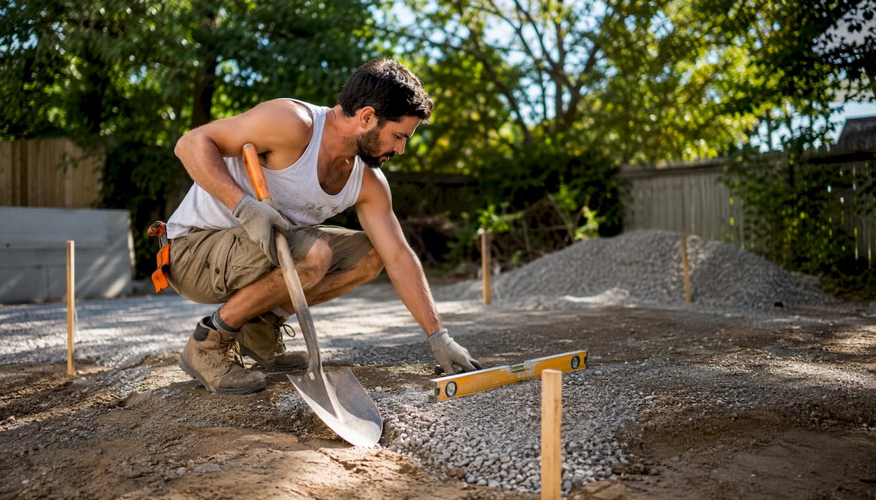 Man grading driveway base with tools outdoors