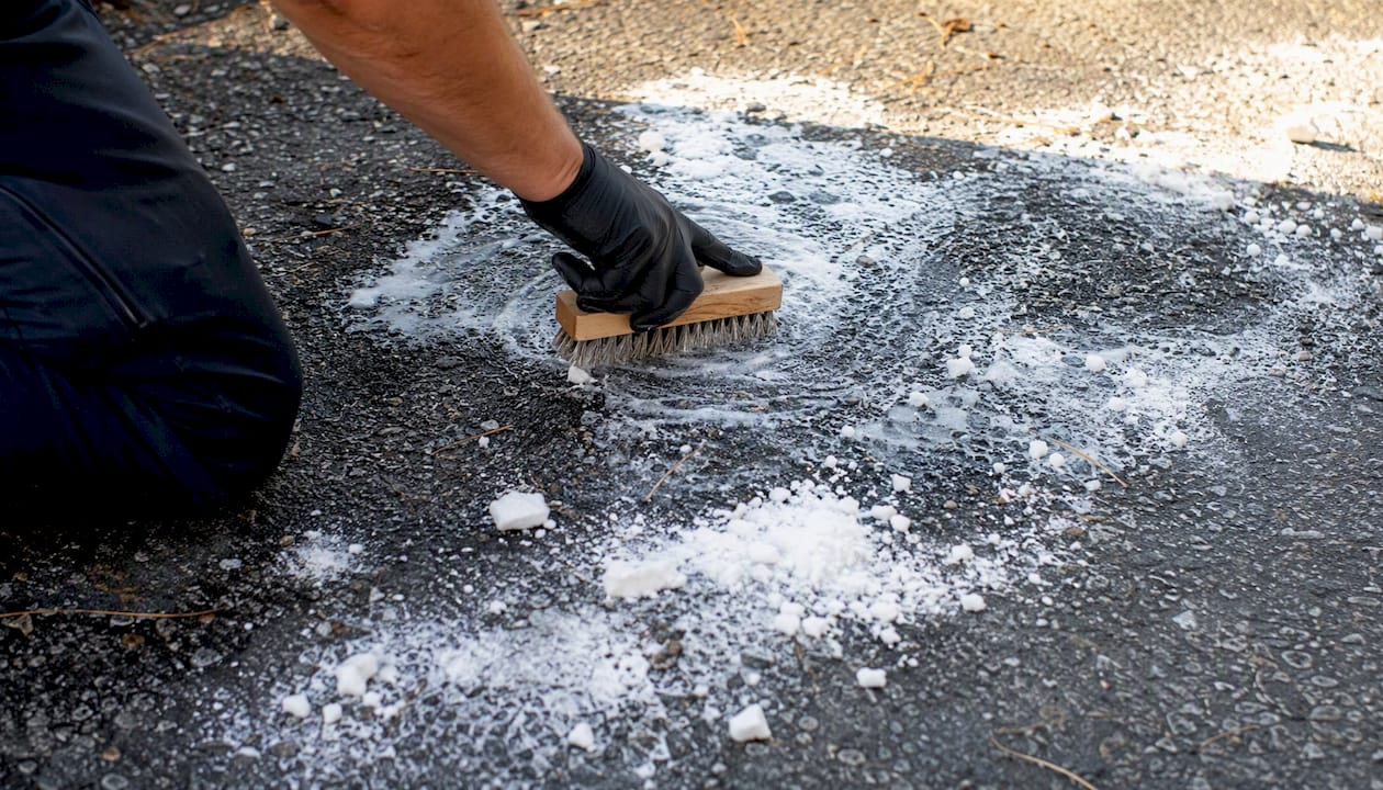 Hand scrubbing baking soda into oil stain on asphalt