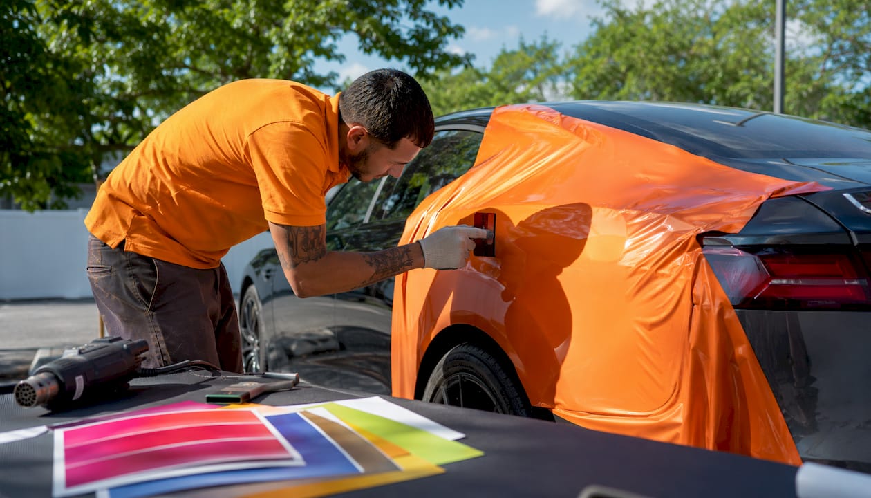 Installer applying vinyl wrap on vehicle door, close-up hands