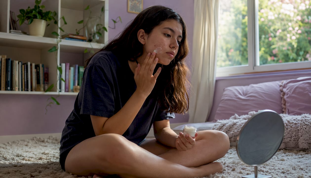 Teenage girl applying acne cream in bedroom