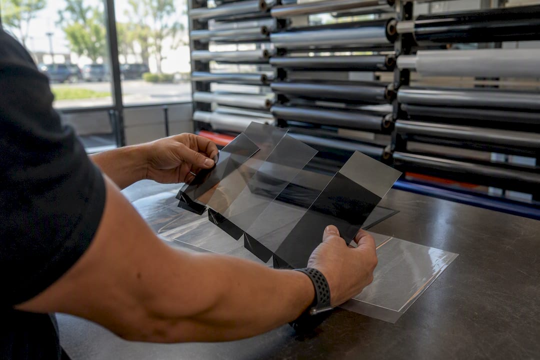 Hands comparing window tint samples at pricing counter