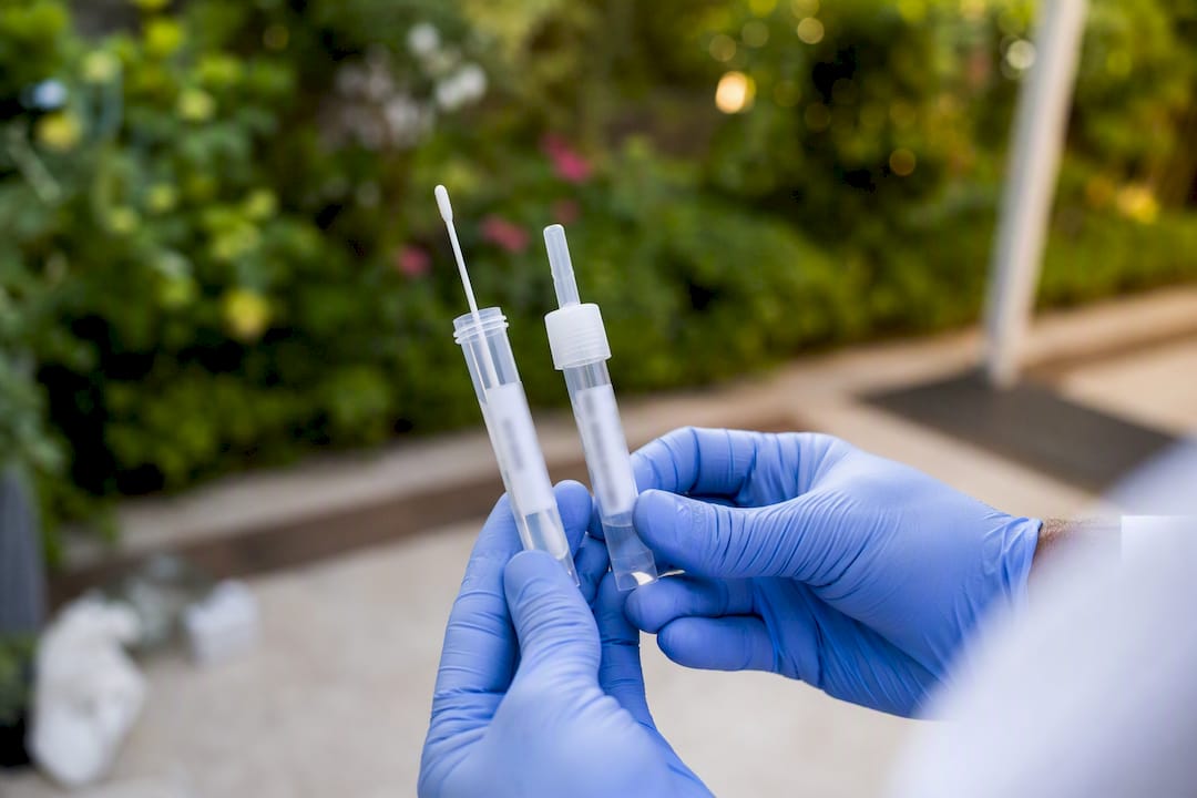 Hands holding PCR and rapid antigen sample swabs