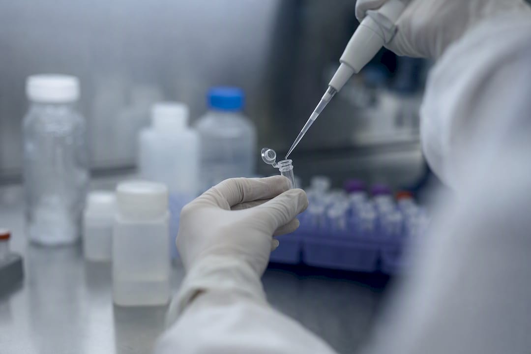 Gloved hands pipetting reagent into PCR tube