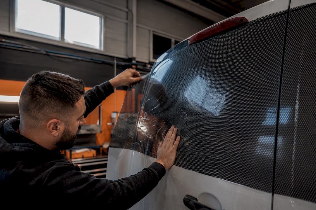 Hands applying vinyl wrap on rear window of commercial van