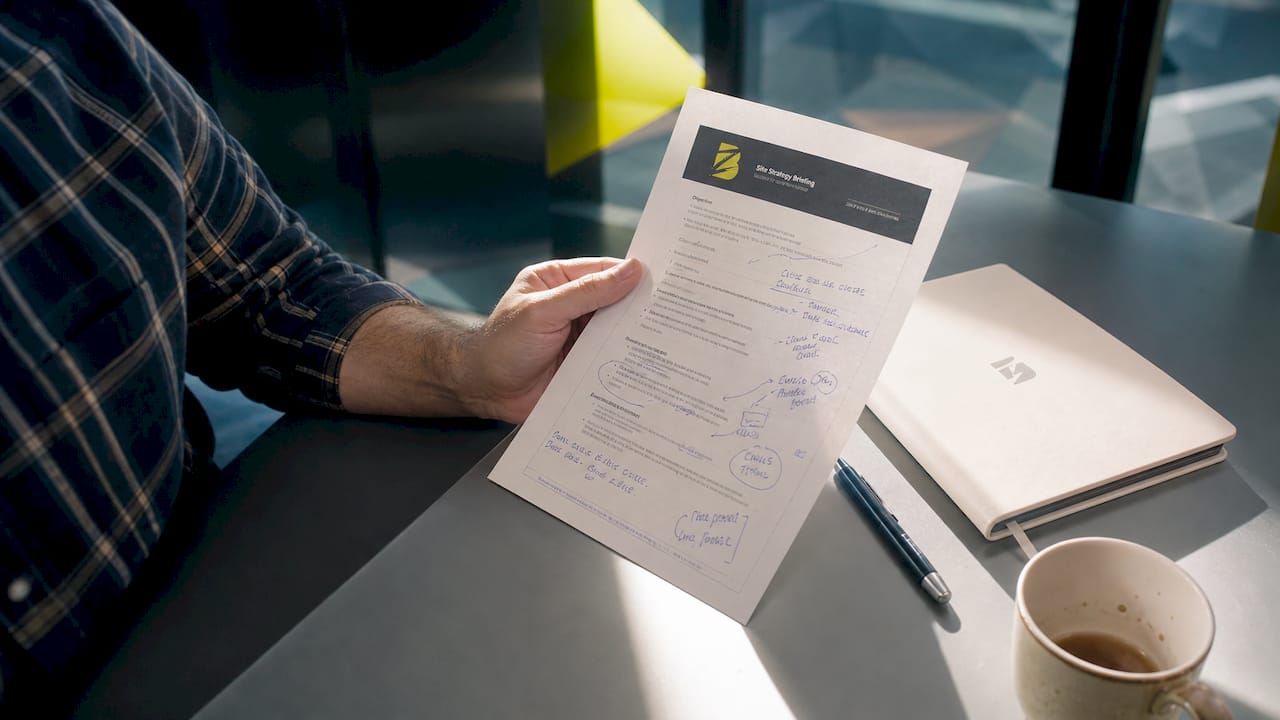 Un dossier de présentation entre les mains, posé sur le bureau au travail.