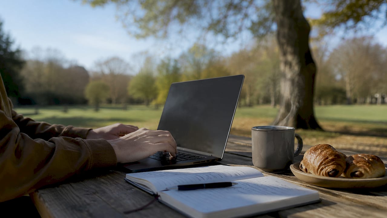Des mains qui s’activent sur le clavier d’un ordinateur portable, installées tranquillement dans l’ambiance chaleureuse d’un café.