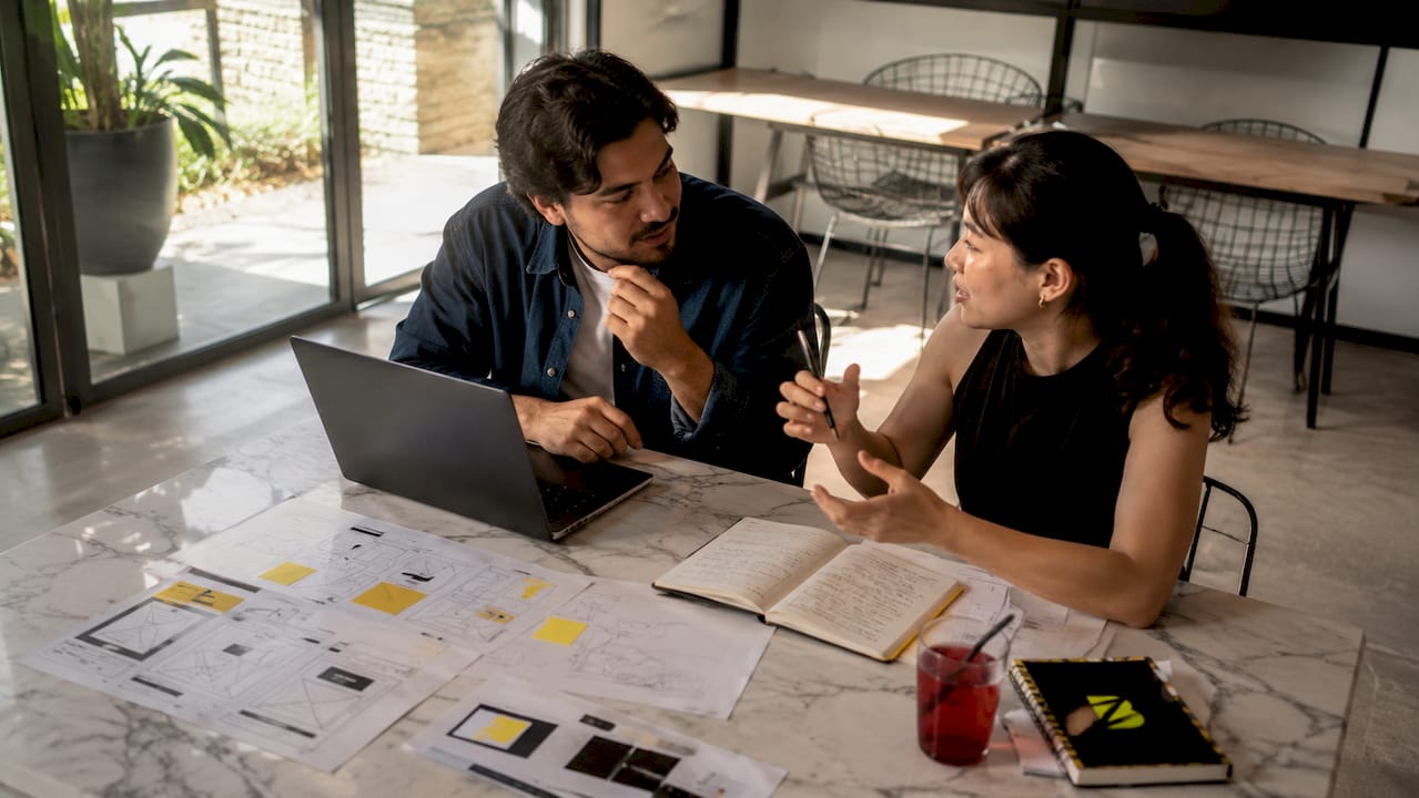 Des collègues échangent autour des différents formats de contenu, installés à la terrasse d’un café.