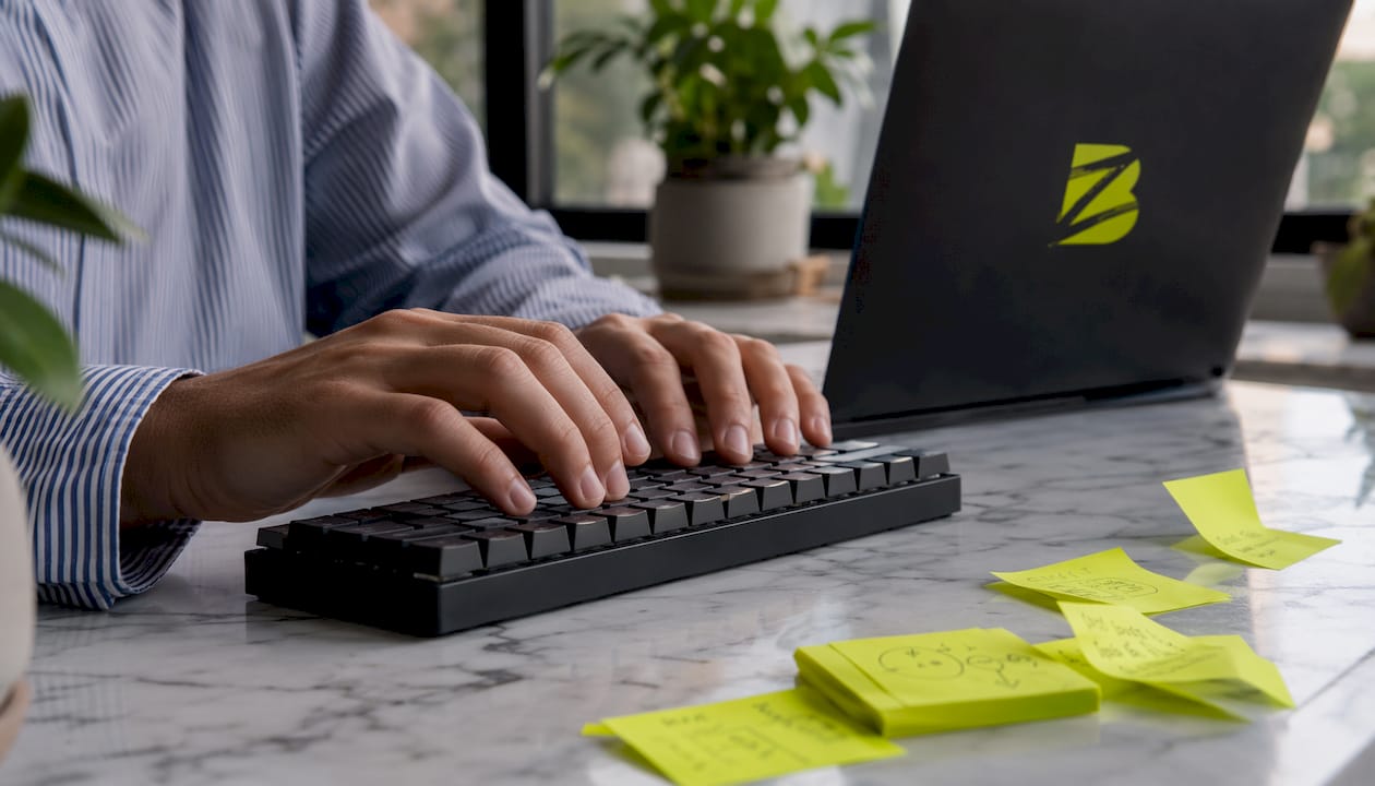 Des mains en train de taper sur un clavier, entourées de post-it colorés.
