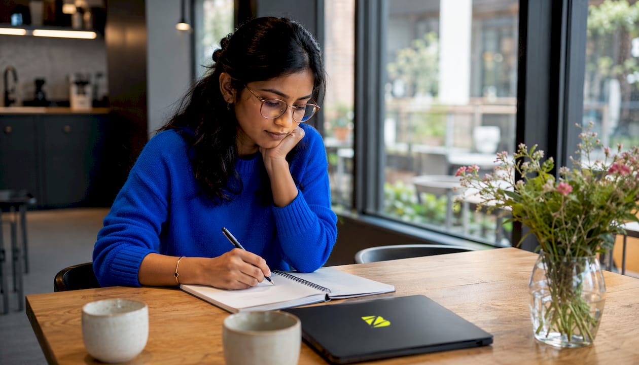 Profil d’une femme concentrée en train de rédiger des accroches publicitaires pour une campagne SEA, carnet à la main.