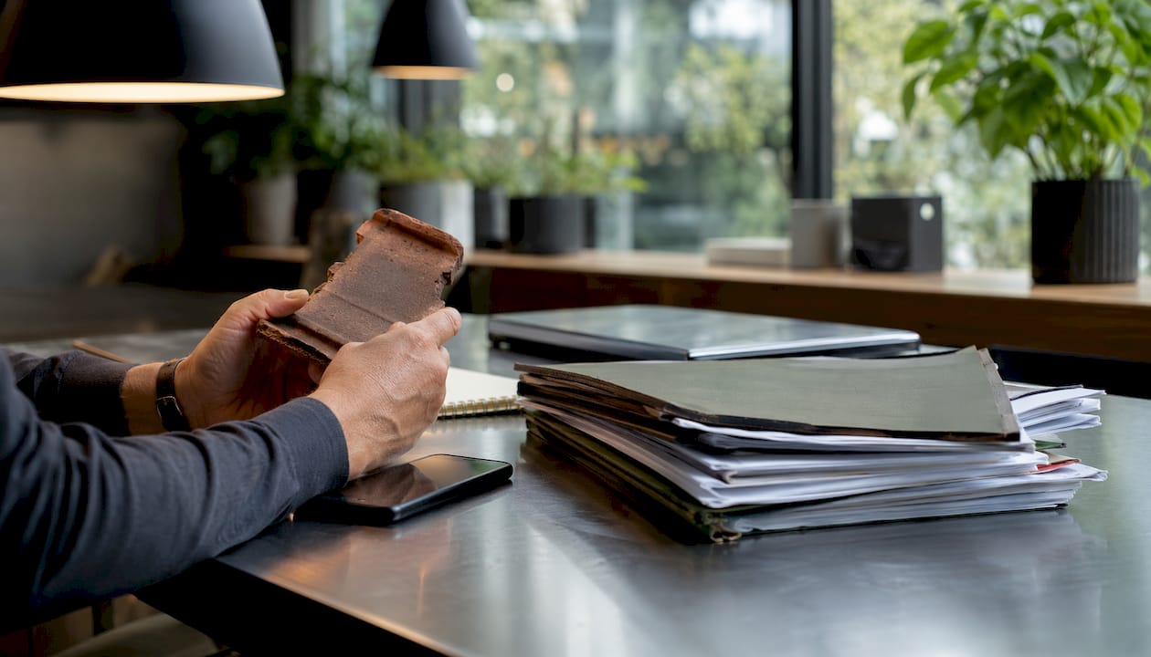 Des mains tiennent un morceau de tuile cassée et des documents d’assurance.