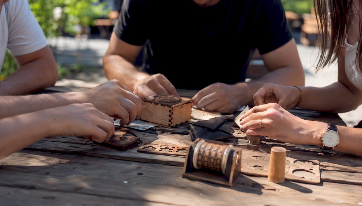 Des mains en pleine réflexion tentent de résoudre une énigme lors d’un escape game en plein air.