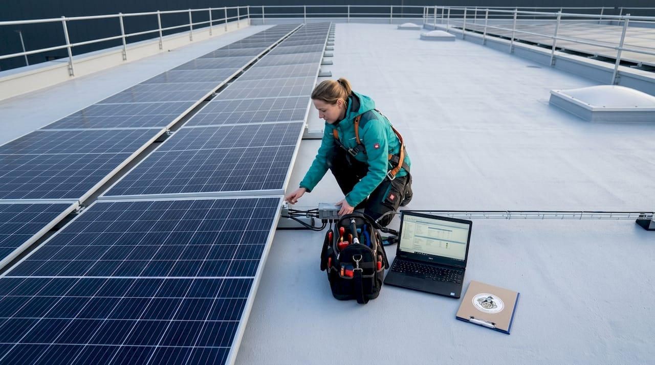 Eine Technikerin montiert Solarmodule auf dem Dach einer Industriehalle.