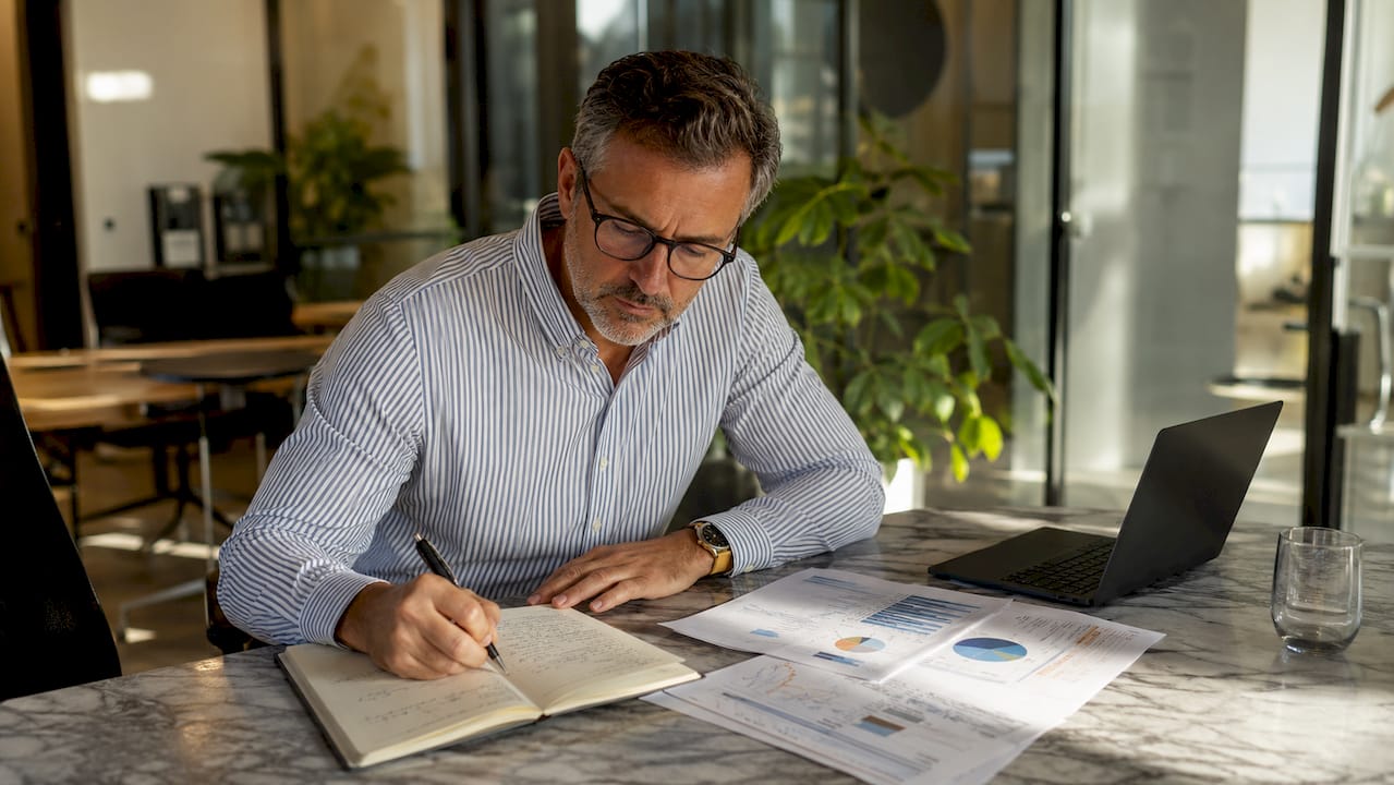 Un homme plongé dans l’analyse de documents financiers, installé à la terrasse d’un café.