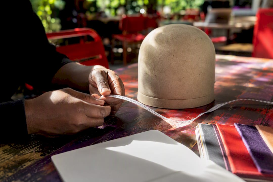 Hands measuring with tape near hat form