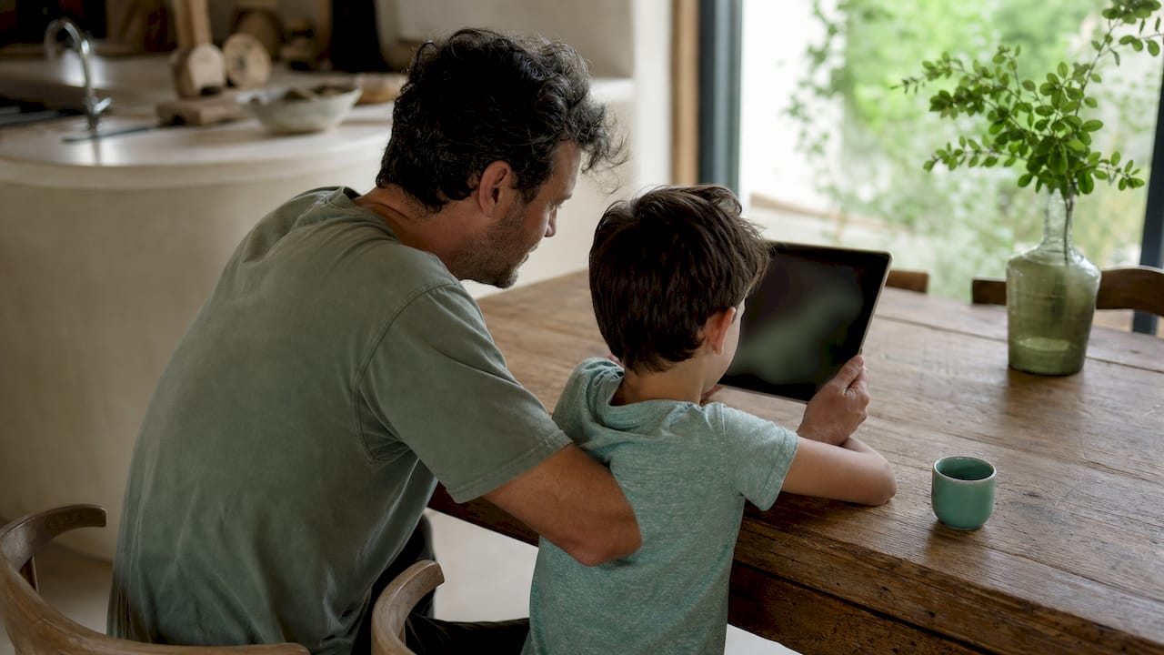 Father explaining screen time rules to son on sofa