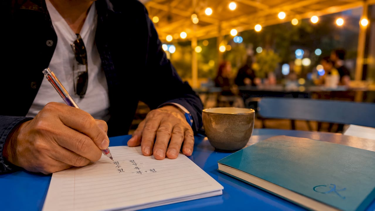 Hands writing Korean Hangul characters