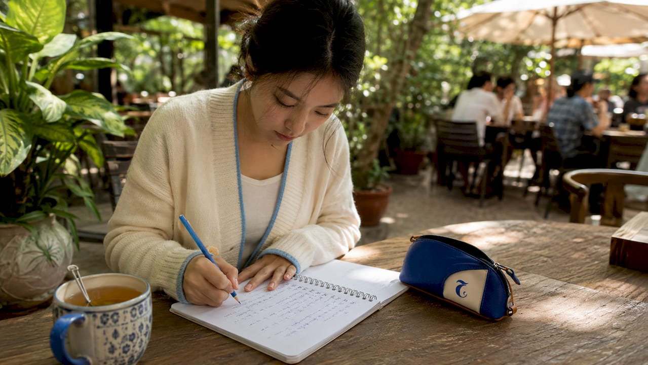 Close-up of hands writing Thai script in notebook