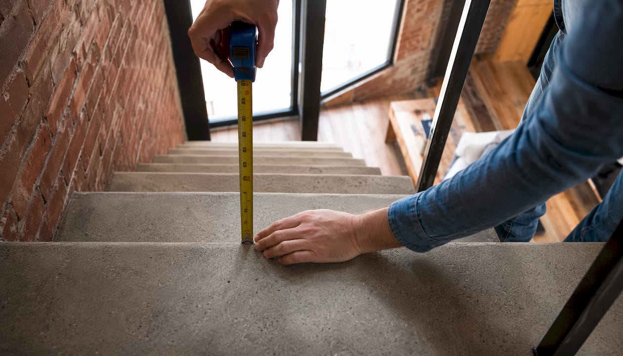 Hands measuring stair rise and run with tape