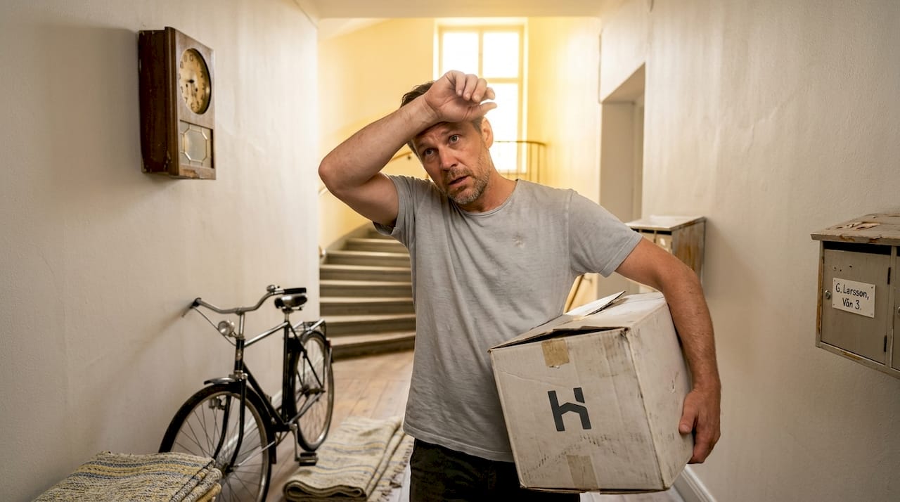En hyresgäst bär en flyttlåda genom en sliten korridor i huset.