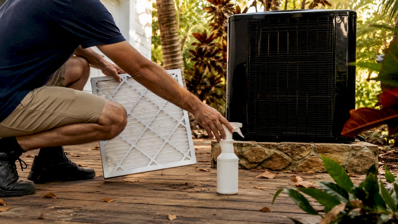 Hands holding HVAC air filter and cleaning condenser coil