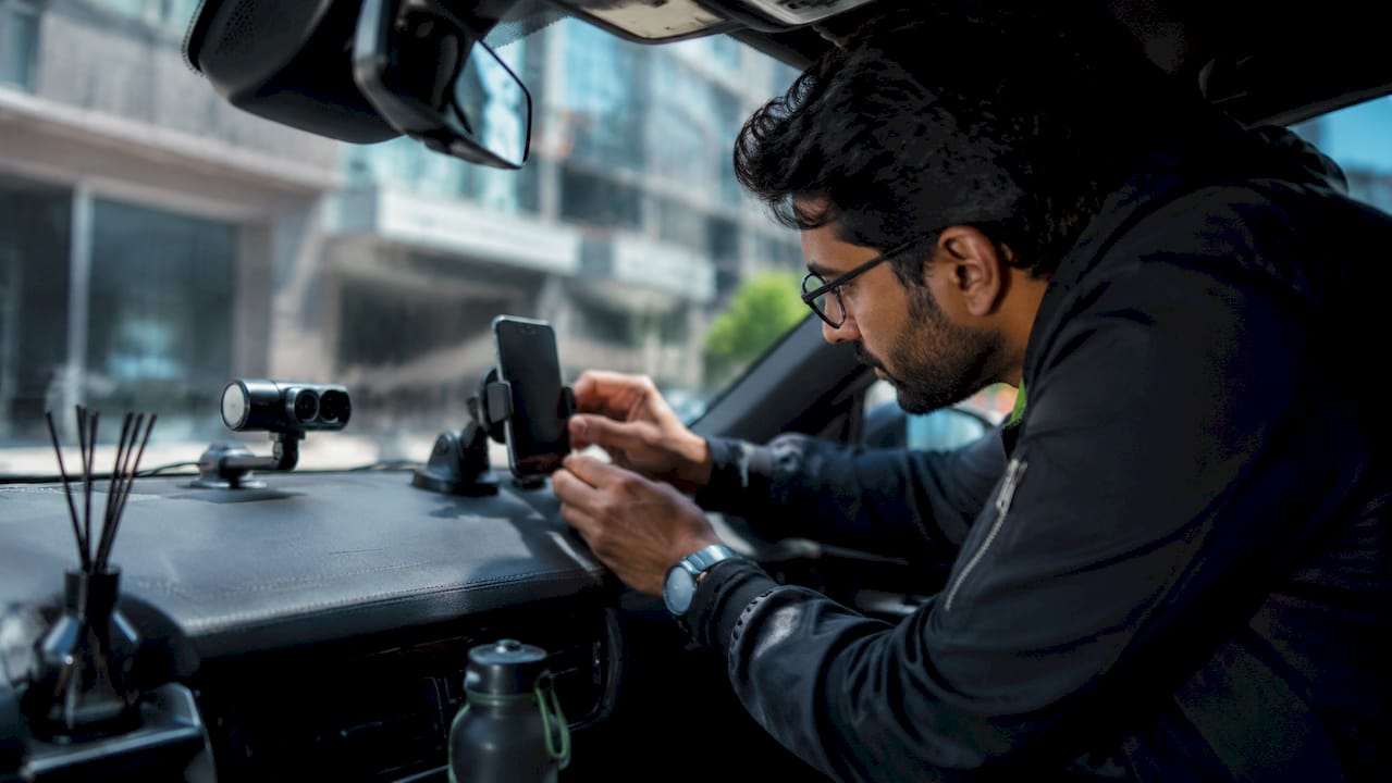 Man adjusting dual SIM phone on car dashboard with dashcam