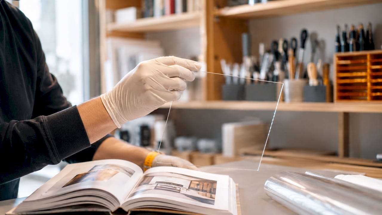 Une main protégée par un gant tient un panneau de verre recouvert d’un film transparent anti-UV.
