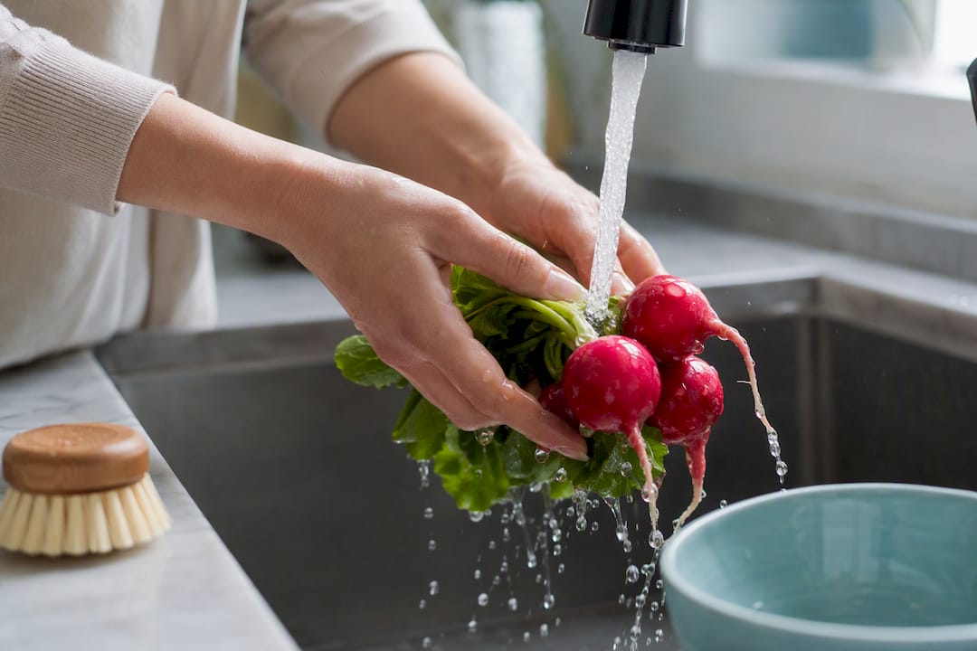 Hands rinsing radishes under running water
