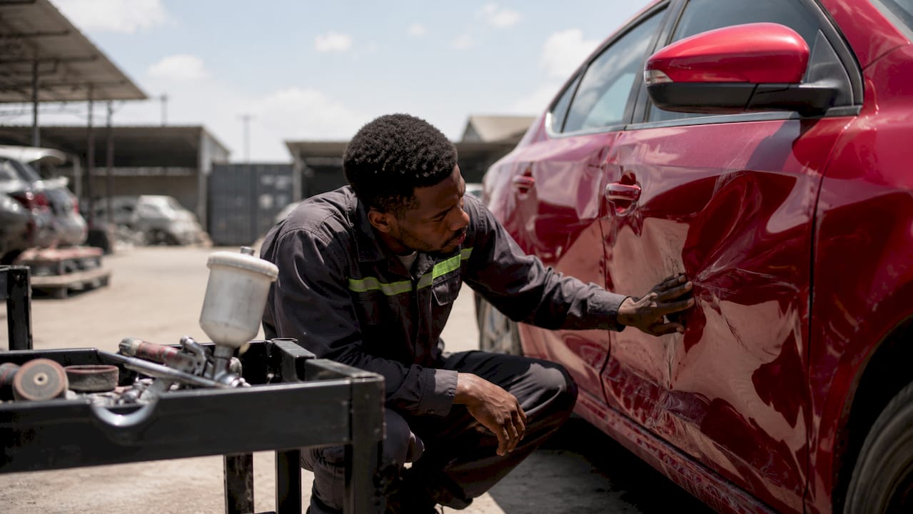 Mechanic inspecting car collision damage in garage