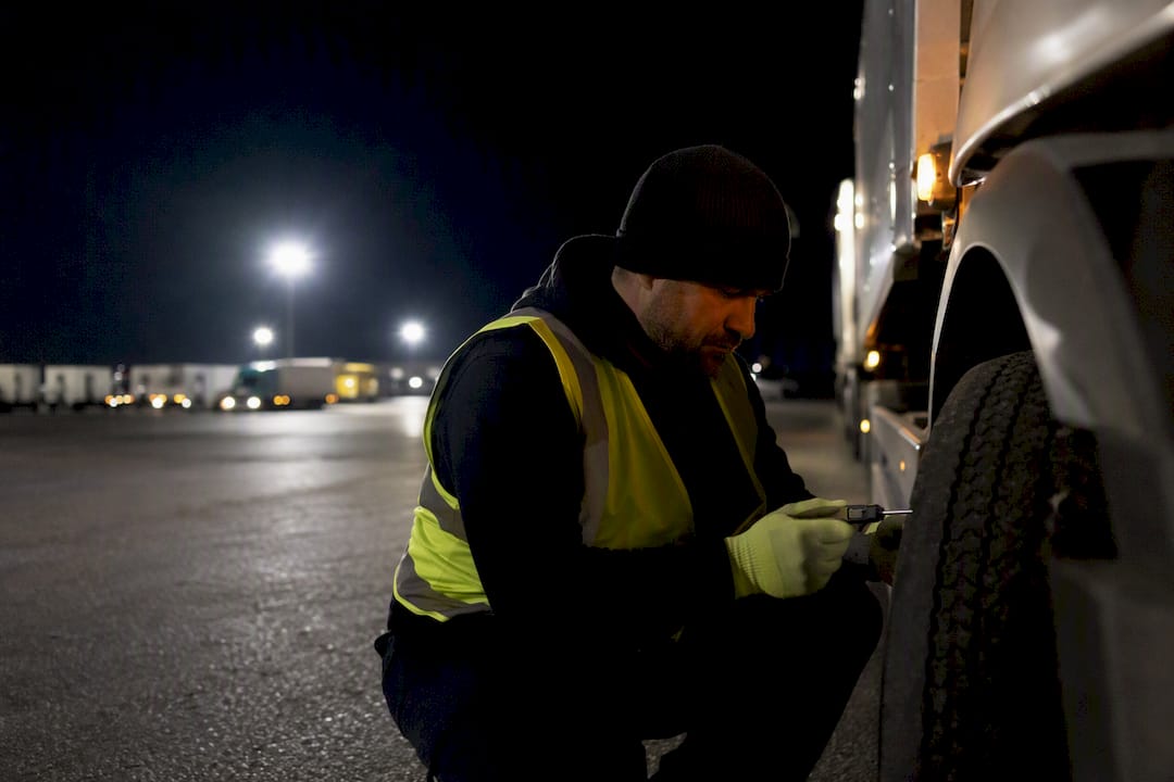Driver checking truck tire tread at night