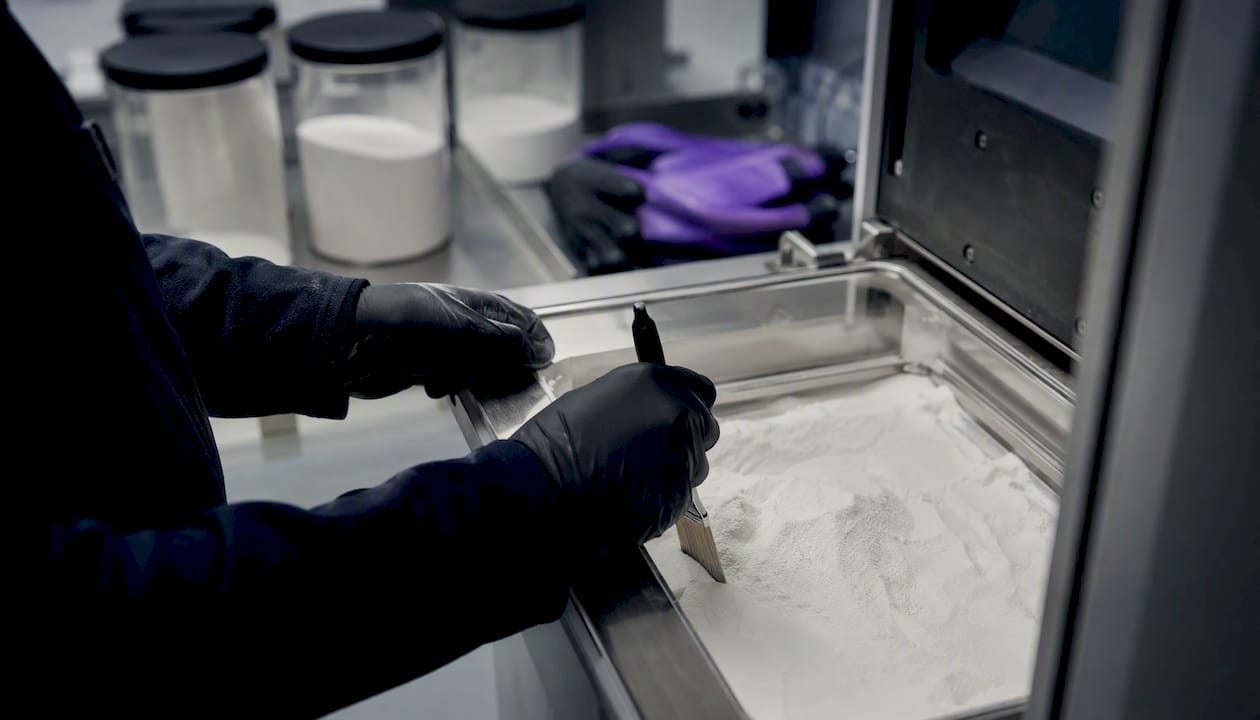 Un technicien s’affaire à préparer le lit de poudre pour une impression 3D.