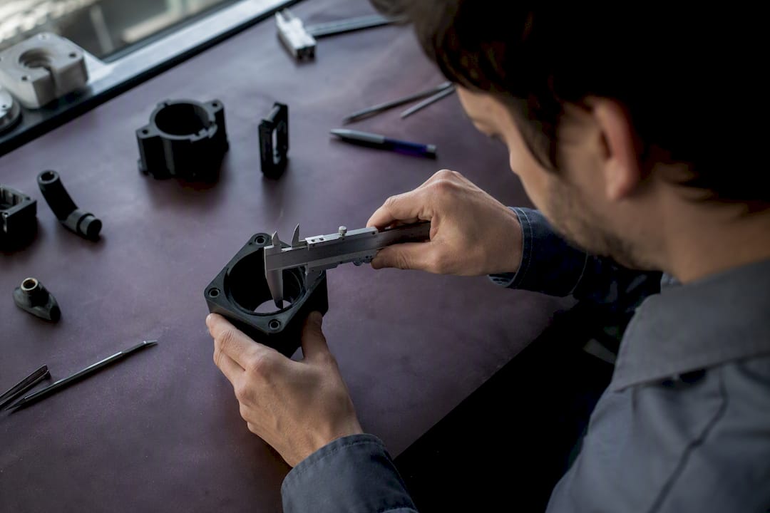 Des mains prennent les mesures de la rainure destinée au joint torique sur une pièce réalisée en impression 3D.