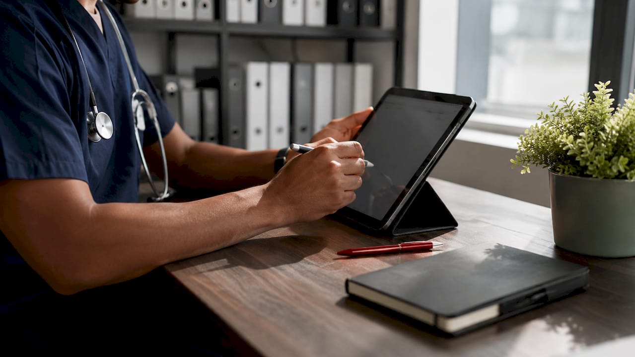 Unas manos introducen datos en una tablet dentro de una consulta médica.